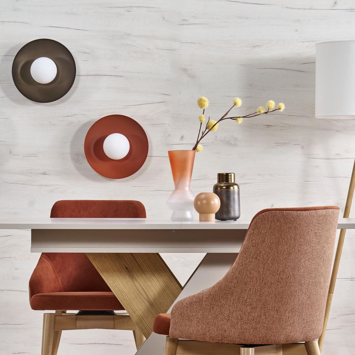 Czarny kinkiet Slate 1xG9 z okrągłym, białym kloszem, zamontowany na ścianie. W tle widoczne dekoracyjne talerze oraz nowoczesne meble w odcieniach brązu i beżu, tworzące elegancką aranżację wnętrza.