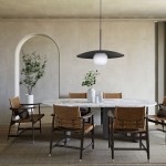 Lampa wisząca Slate w kolorze czarnym z białym kloszem, zawieszona nad okrągłym stołem w jadalni. W tle widoczne drewniane krzesła i rośliny w donicach, na jasnej ścianie. Lampa ma nowoczesny design, z metalowym ramieniem i dużą, okrągłą kulą.