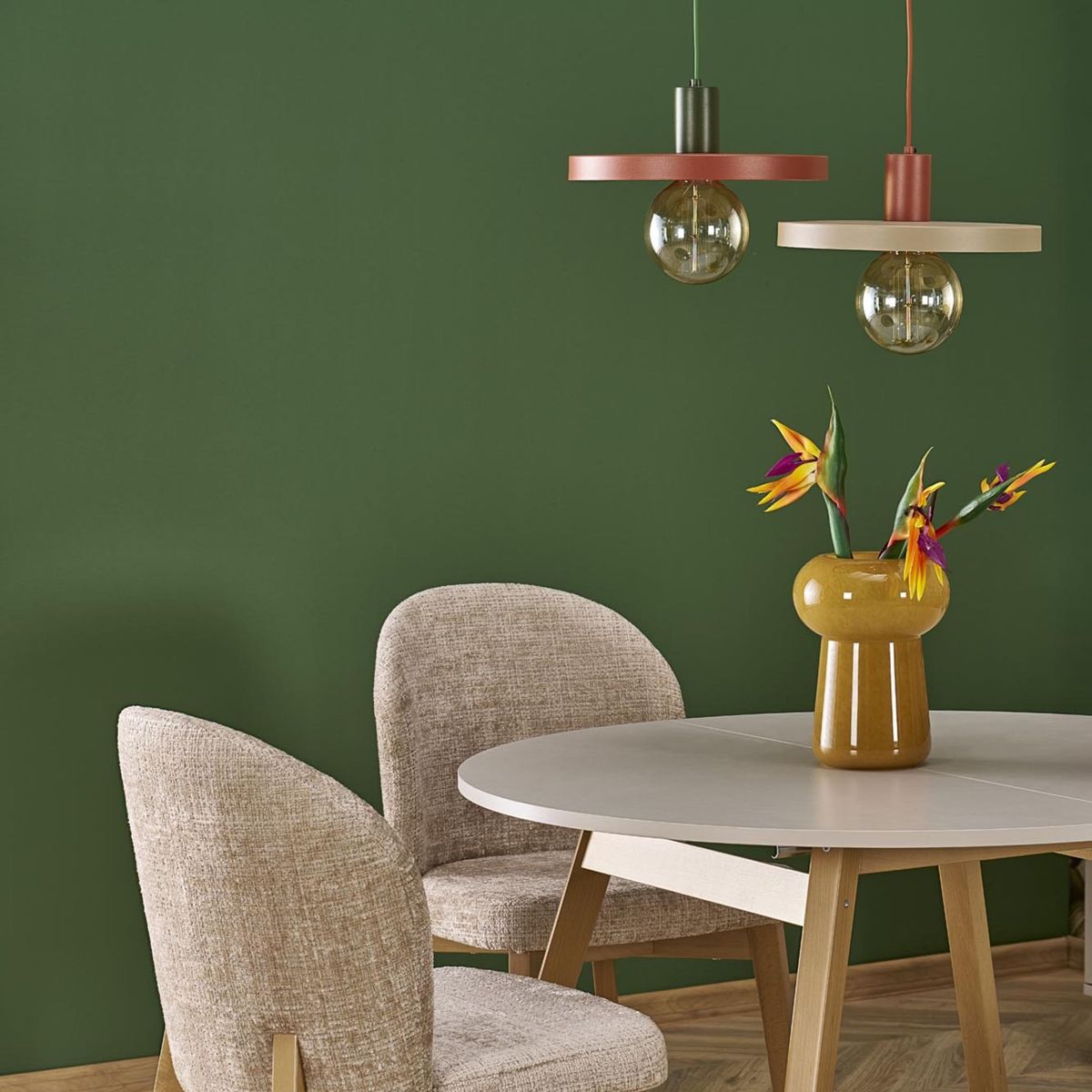 Lampa wisząca Sila D30 z brązowym, ceglastym abażurem, zawieszona nad okrągłym stołem. W tle zielona ściana, a na stole wazon z kolorowymi kwiatami oraz dwa jasnoszare krzesła. Widoczne jedno źródło światła E27.
