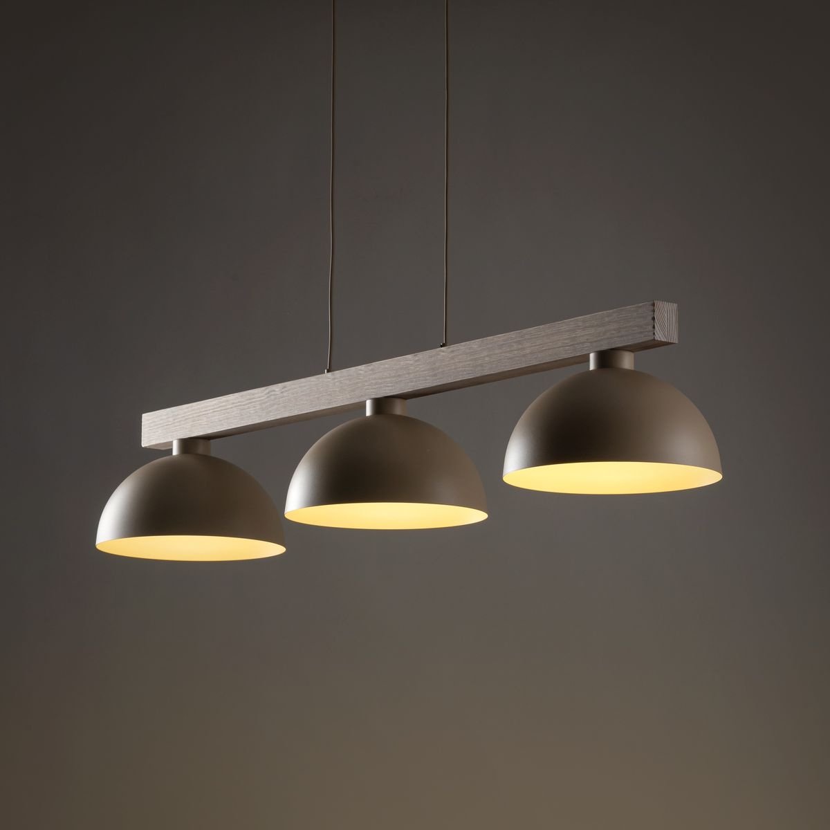 Lampa wisząca Oslo z trzema kloszami w kolorze beżowym, zawieszona na drewnianym stelażu. Klosze mają zaokrąglony kształt i emitują ciepłe światło, idealna do nowoczesnych wnętrz. Ujęcie frontalne, na ciemnym tle.