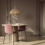 Lampa wisząca Oslo w kolorze jasnego drewna i beżowym kloszu, zawieszona nad okrągłym stołem. W tle widoczne dwa różowe krzesła i minimalistyczne wnętrze. Kąt ujęcia frontalny, zbliżenie na detal lampy oraz otoczenie.