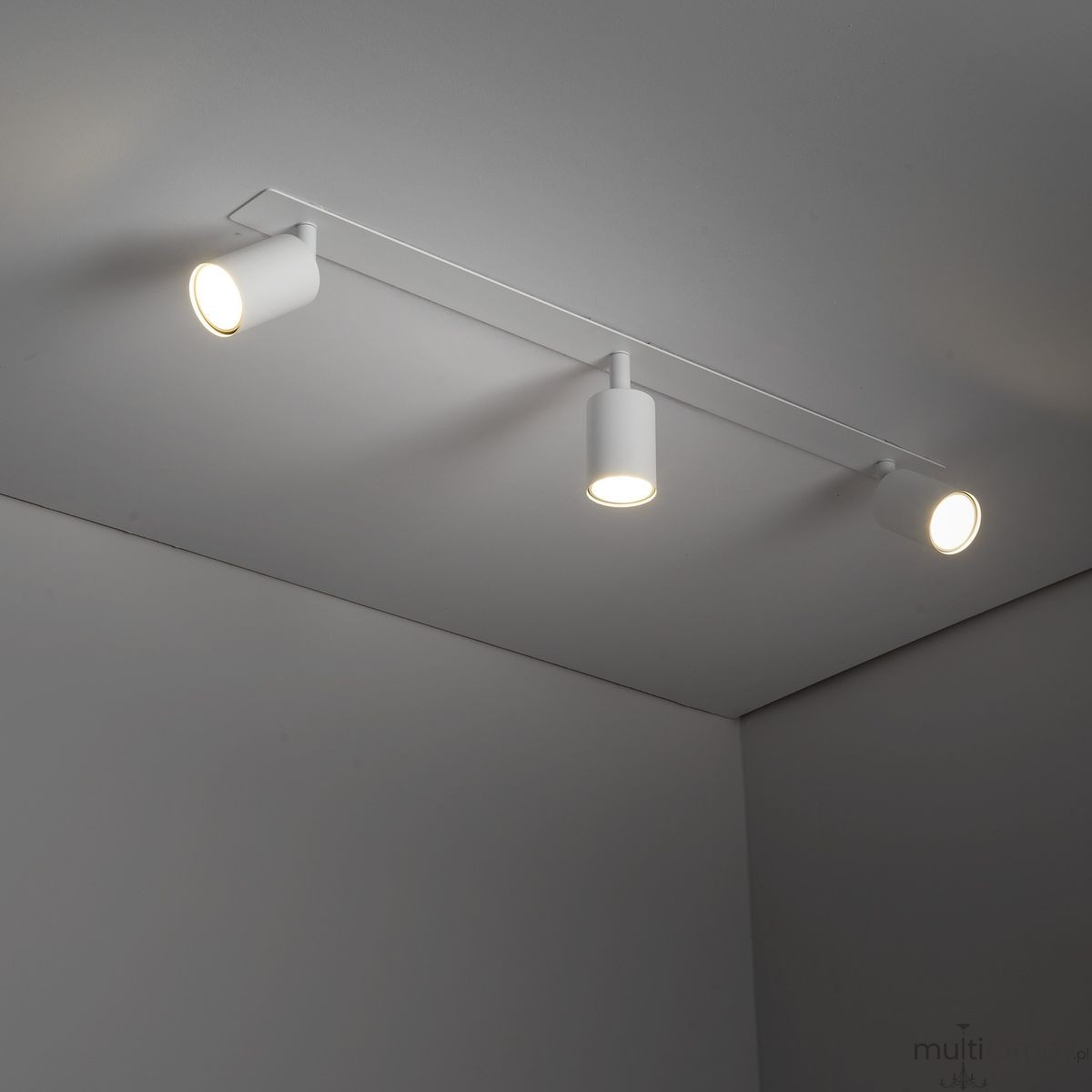 Lampa sufitowa podtynkowa Nex, kolor biały, z trzema oprawami na żarówki GU10. Zamontowana na płaskiej, prostokątnej podstawie, z widocznymi reflektorami w kształcie cylindrów. Oświetlenie skierowane w dół, na jednolitym tle.