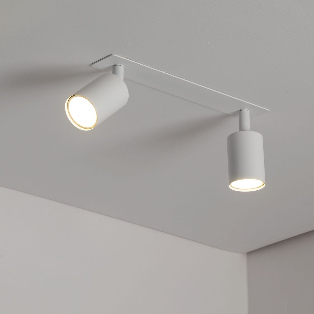 Lampa sufitowa podtynkowa Nex w kolorze białym, z dwoma punktami świetlnymi GU10. Ujęcie z dołu, ukazujące cylindryczne klosze z jasnym światłem. Montowana na prostokątnej podstawie, na tle gładkiego sufitu.