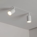 Lampa sufitowa podtynkowa Nex w kolorze białym, z dwoma punktami świetlnymi GU10. Ujęcie z dołu, ukazujące cylindryczne klosze z jasnym światłem. Montowana na prostokątnej podstawie, na tle gładkiego sufitu.