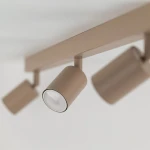 Lampa sufitowa spot Nex w kolorze beżowym z czterema reflektorami GU10. Ujęcie z boku, ukazujące cylindryczne oprawy świetlne zamocowane na prostokątnej podstawie. Gładka, matowa powierzchnia.