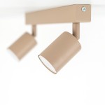 Beżowa lampa sufitowa typu spot z dwoma ruchomymi oprawami na żarówki GU10, zamontowana na prostokątnej listwie. Ujęcie z boku, podkreślające cylindryczny kształt reflektorów. Tło jednolite, białe.