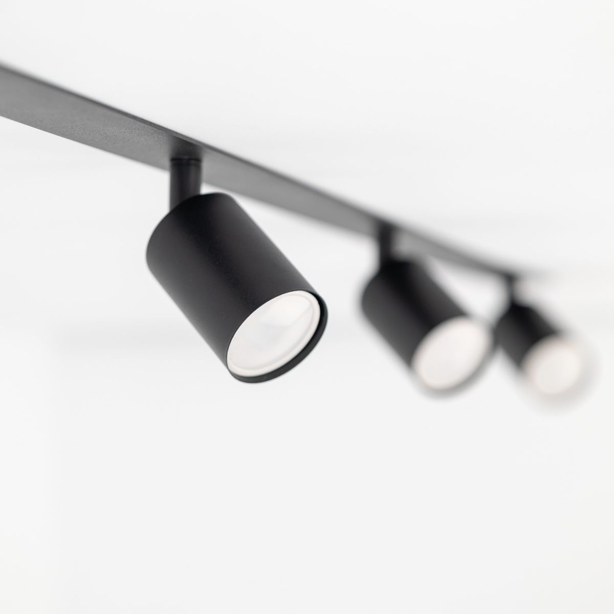 Czarna lampa sufitowa podtynkowa Nex z czterema oprawami GU10, zamontowana na prostokątnej listwie. Ujęcie z boku, ukazujące dwa okrągłe reflektory z matowym wykończeniem. Tło jasne, proste, co podkreśla minimalistyczny design lampy.