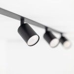 Czarna lampa sufitowa podtynkowa Nex z czterema oprawami GU10, zamontowana na prostokątnej listwie. Ujęcie z boku, ukazujące dwa okrągłe reflektory z matowym wykończeniem. Tło jasne, proste, co podkreśla minimalistyczny design lampy.