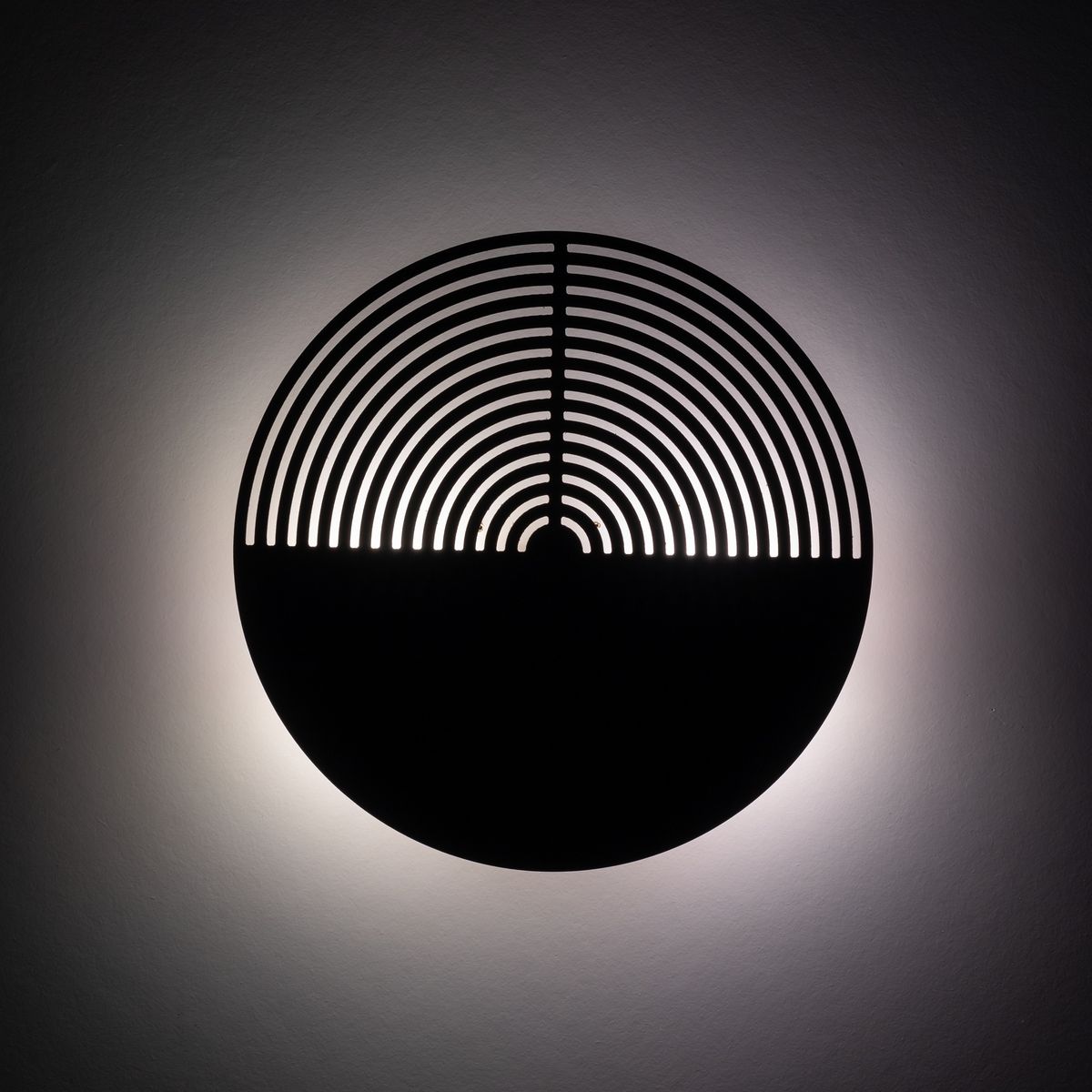 Kinkiet Lunar Wood w formie okrągłej lampy, wykonany z drewna, z wyciętymi wzdłużnymi wzorami. Oświetlenie emituje delikatne światło w tle, z mocowaniem do ściany, idealne do nowoczesnych wnętrz.