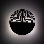 Kinkiet Lunar Wood w formie okrągłej lampy, wykonany z drewna, z wyciętymi wzdłużnymi wzorami. Oświetlenie emituje delikatne światło w tle, z mocowaniem do ściany, idealne do nowoczesnych wnętrz.