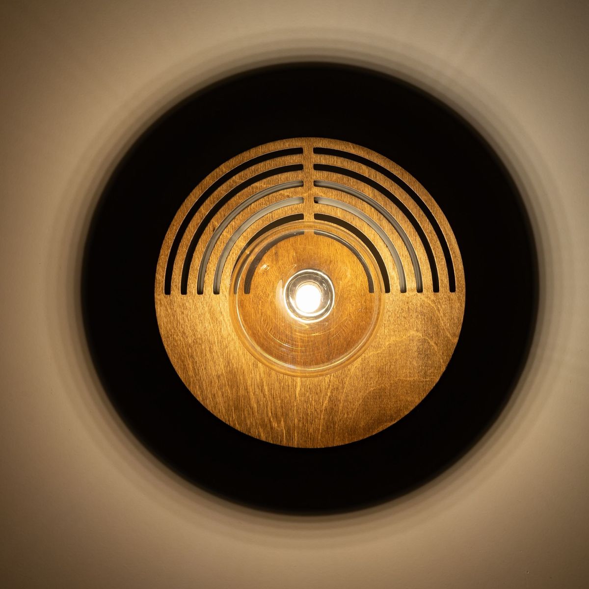 Kinkiet Lunar Wood D30 z drewna w kształcie okręgu, z wycięciami w formie fal. Widoczna żarówka G9 w centrum. Ujęcie z góry, na jednolitym tle, podkreślające naturalną fakturę drewna i subtelne oświetlenie.