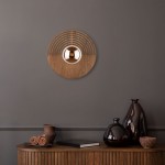 Kinkiet Lunar Wood D30 w kolorze drewna z okrągłą podstawą z wypukłym elementem w centralnej części. Ułożony na szarej ścianie, na tle drewnianego stolika z dekoracyjnymi naczyniami i książkami.