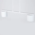 Lampa wisząca Mila w kolorze białym z dwoma oprawami na żarówki GX53. Prosta, minimalistyczna konstrukcja z poziomą belką i dwiema cylindrycznymi kloszami. Zawieszona na dwóch kablach na jednolitym tle.