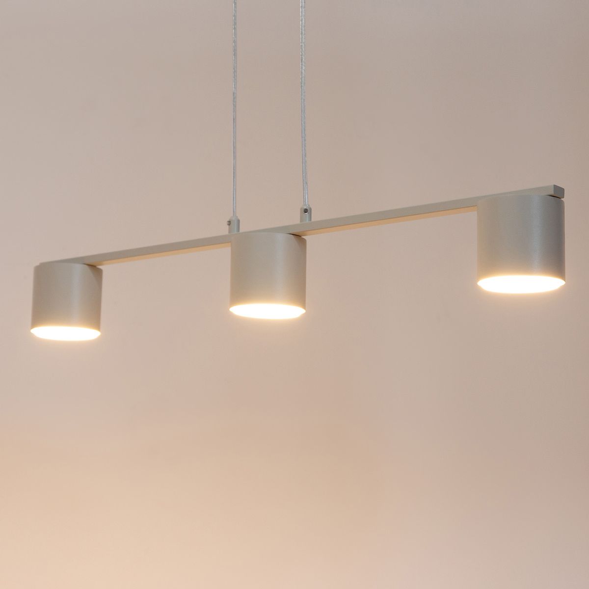 Lampa wisząca Mila w kolorze szaro-beżowym, z trzema okrągłymi kloszami na żarówki GX53. Ujęcie frontalne, produkt zawieszony na dwóch cienkich linach, emitujący ciepłe światło. Minimalistyczny design, idealna do nowoczesnych wnętrz.