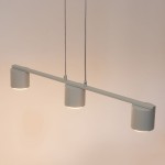 Lampa wisząca Mila w kolorze szarym beżowym, z trzema okrągłymi kloszami, zawieszona na cienkich linkach, umieszczona na prostokątnej podstawie. Klosze mają delikatne, matowe wykończenie i emitują ciepłe światło.