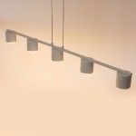 Lampa wisząca Mila w kolorze szaro-beżowym z pięcioma cylindrycznymi kloszami, zawieszona na prostym, metalowym stelażu. Klosze skierowane w dół, zawieszenie na dwóch sznurach. Na tle jasnym, minimalistyczny design.