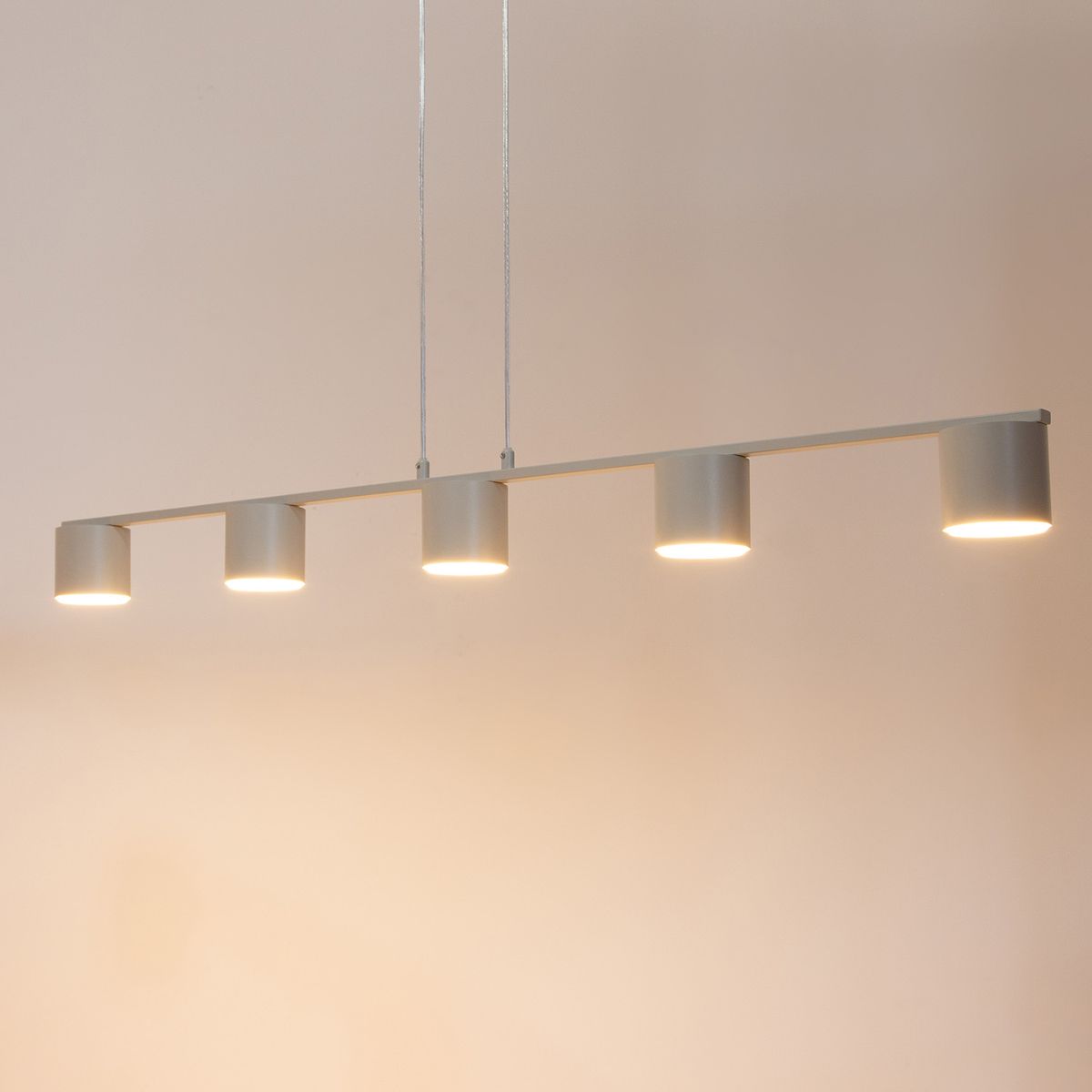 Lampa wisząca Mila w kolorze szarym beż, składająca się z pięciu okrągłych źródeł światła, zawieszona na cienkich linkach. Prosty, nowoczesny design, z równomiernym rozłożeniem lamp, idealna do oświetlenia wnętrz.