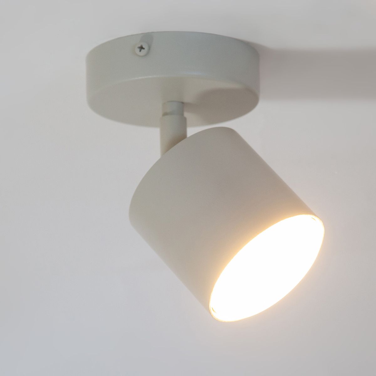 Kinkiet Mila w kolorze szaro-beżowym, z pojedynczym źródłem światła GX53. Okrągła głowica lampy nachylona w dół, zamontowana na okrągłej podstawie. Prosty, minimalistyczny design.