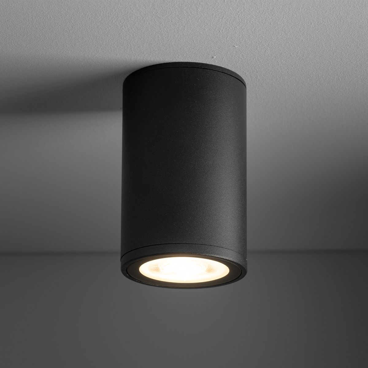 Lampa sufitowa Flare w kolorze czarnym, cylindryczna, z jedną oprawą GU10. Zawieszona na suficie, z widocznym źródłem światła, odpowiednia do użytku na zewnątrz dzięki klasie IP44.