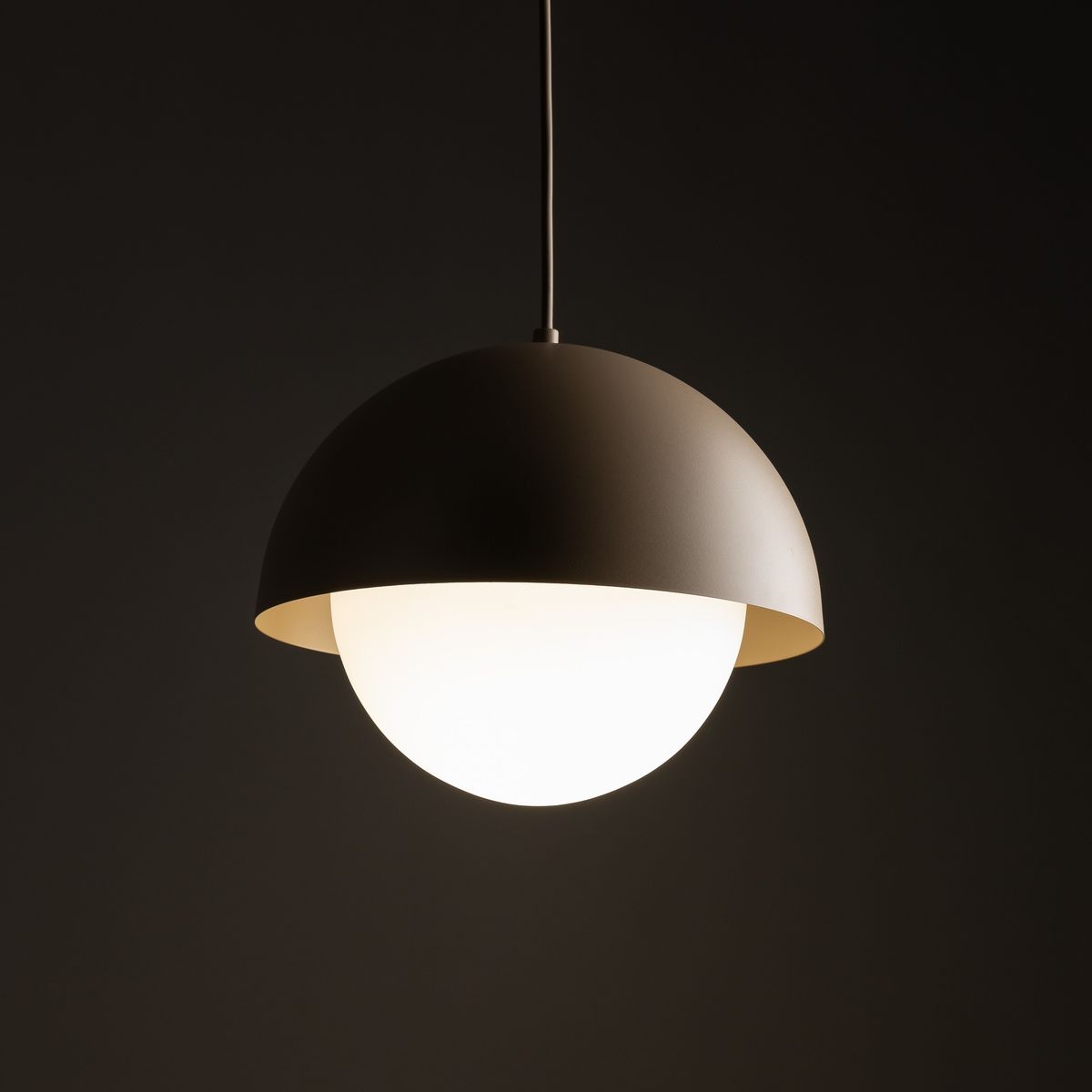Lampa wisząca Bono D27 z kloszem w kształcie półkuli, w kolorze brązowym. Posiada białą, szklana kulę emitującą światło. Zawieszona na cienkim przewodzie, widoczna na ciemnym tle. Wykonana z matowego metalu. Idealna do nowoczesnych wnętrz.