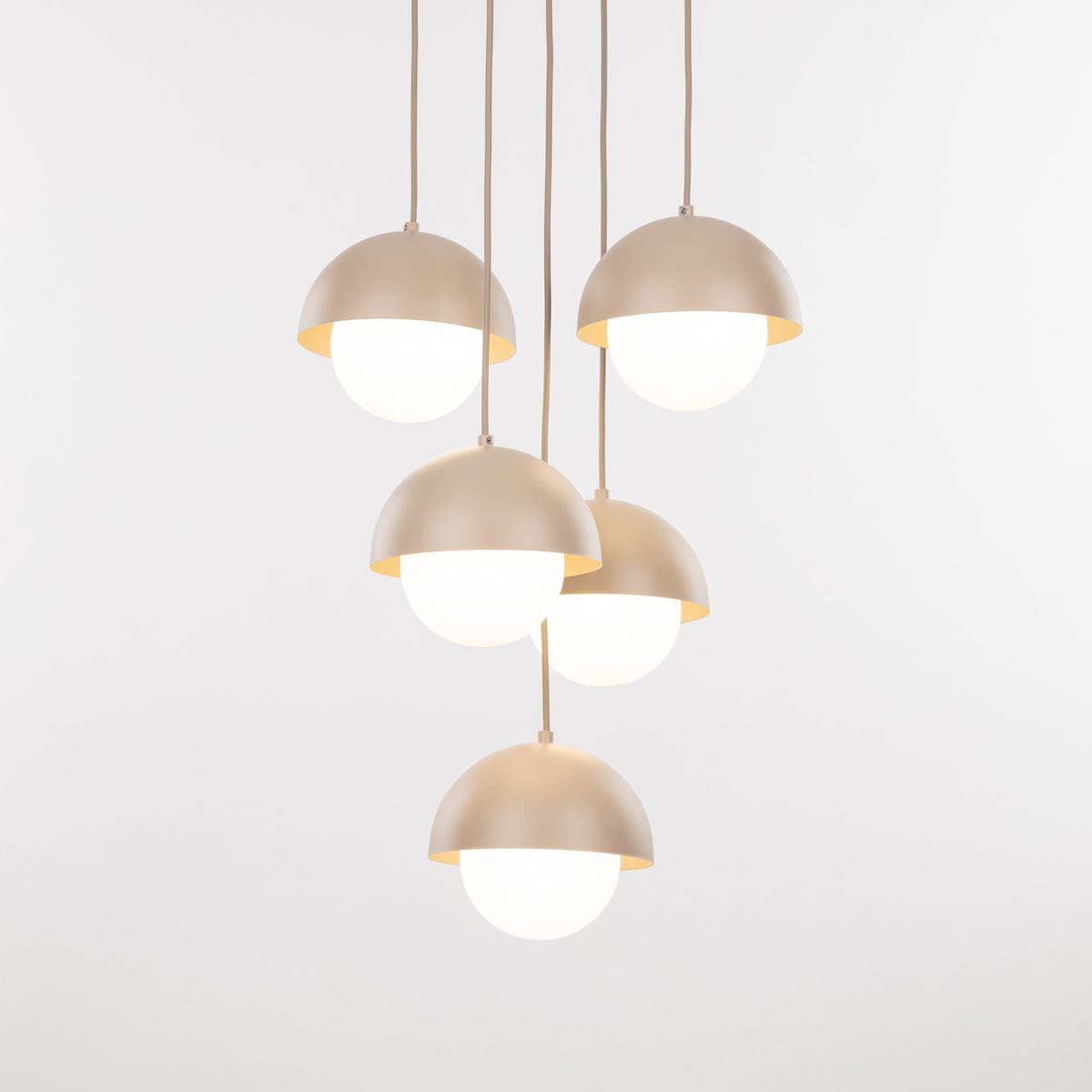Lampa wisząca Bono z pięcioma kloszami G9 w kształcie półkul, w kolorze matowego beżu z białymi szklanymi osłonami. Zawieszona na długich przewodach, idealna do nowoczesnych wnętrz. Tło proste, białe.