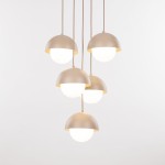 Lampa wisząca Bono z pięcioma kloszami G9 w kształcie półkul, w kolorze matowego beżu z białymi szklanymi osłonami. Zawieszona na długich przewodach, idealna do nowoczesnych wnętrz. Tło proste, białe.