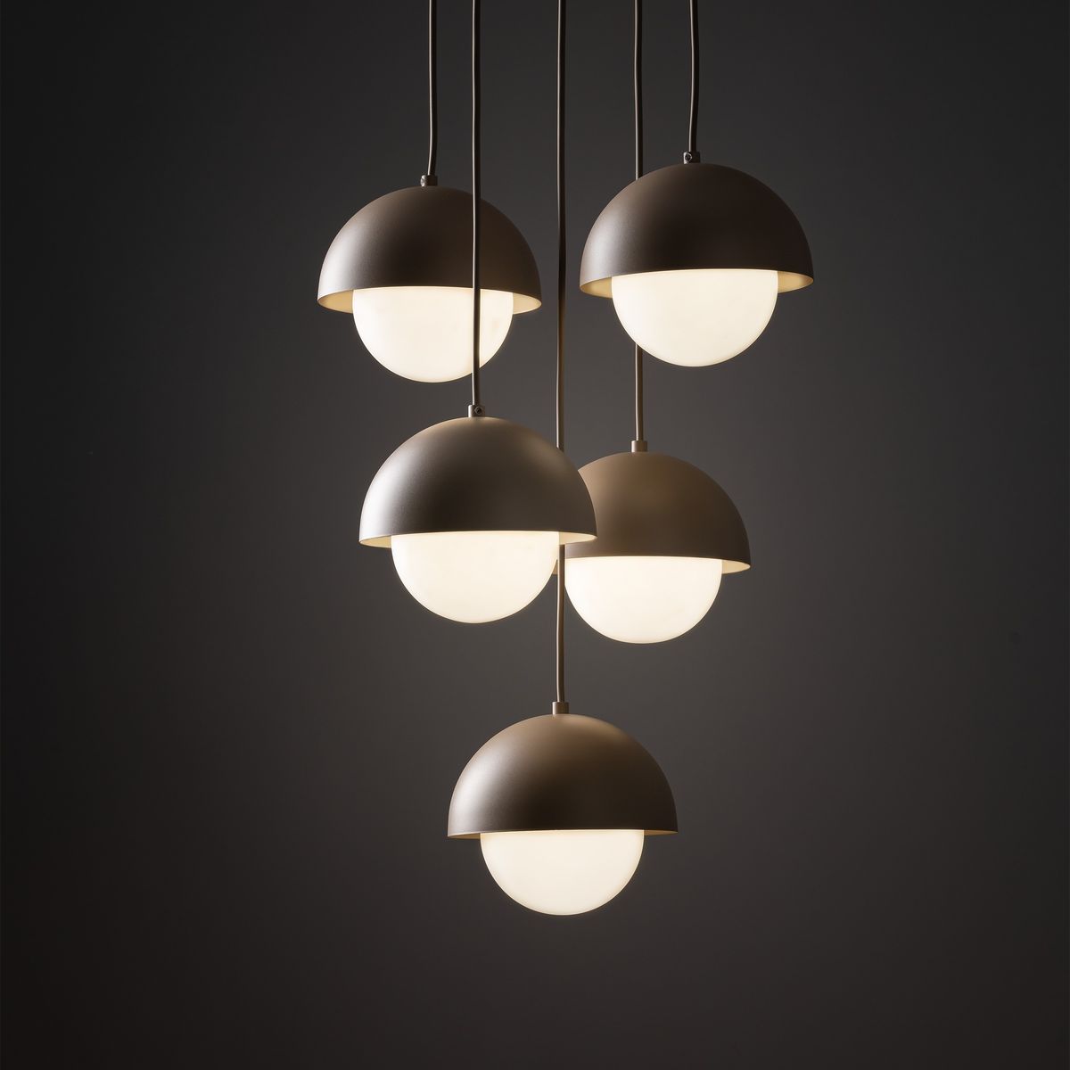 Lampa wisząca Bono z pięcioma kloszami w kształcie półkul, w kolorze matowej szarości, z białymi szklanymi kulami. Zawieszona na cienkich linkach, w minimalistycznym stylu, na ciemnym tle. Idealna do nowoczesnych wnętrz.