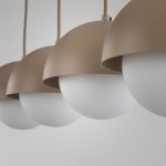 Lampa wisząca Bono z czterema kloszami w kształcie półkul, o matowej beżowej obudowie i białych, szklanych kulach. Produkt zawieszony na cienkich przewodach, ukazany z bliska, na jednolitym tle.
