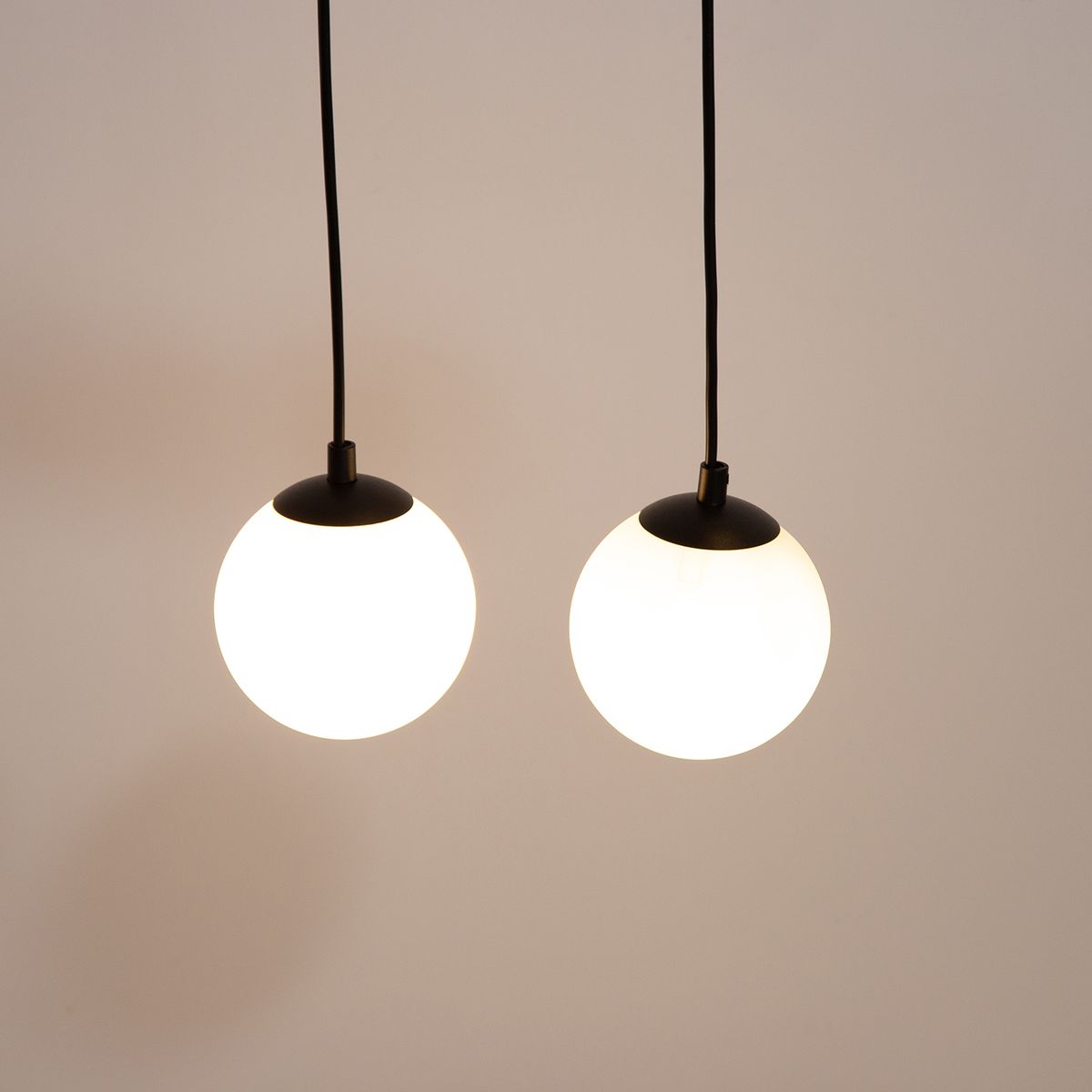 Lampa wisząca Tavira z dwoma okrągłymi kloszami w białym kolorze i czarnymi detalami. Klosze zawieszone na cienkich czarnych przewodach, w równym odstępie od siebie. Prosta, nowoczesna forma, idealna do aranżacji wnętrz.