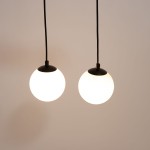 Lampa wisząca Tavira z dwoma okrągłymi kloszami w białym kolorze i czarnymi detalami. Klosze zawieszone na cienkich czarnych przewodach, w równym odstępie od siebie. Prosta, nowoczesna forma, idealna do aranżacji wnętrz.
