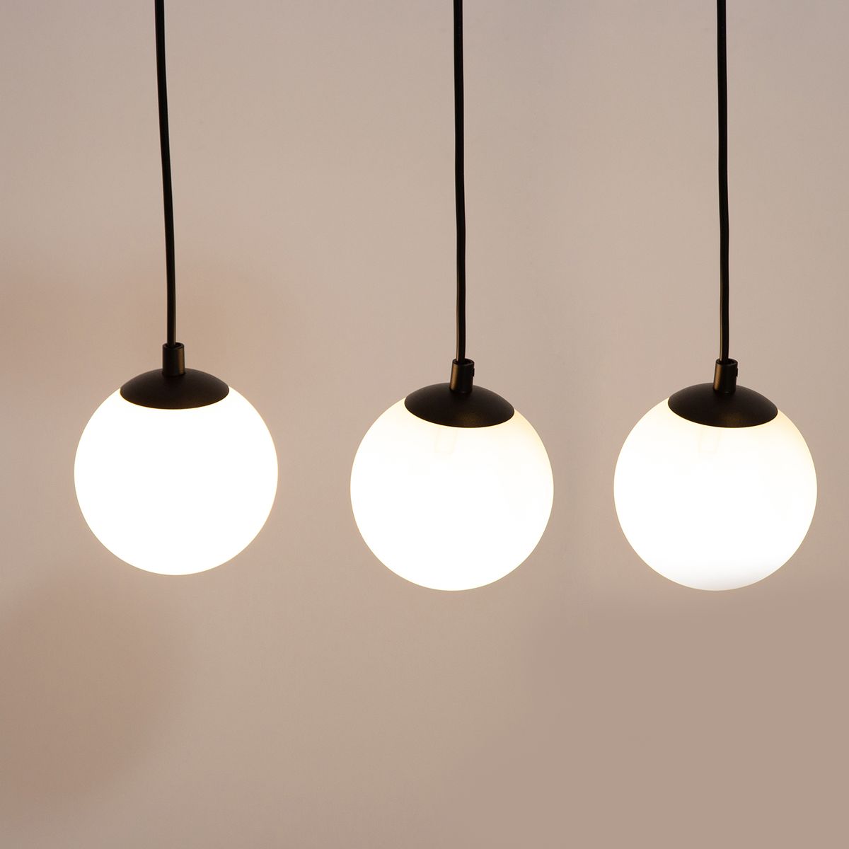 Lampa wisząca Tavira w kolorze czarnym z trzema okrągłymi kloszami ze szkła opalowego, zawieszona na czarnych przewodach. Klosze mają czarne podstawy, a lampa przeznaczona jest do żarówek G9 i GU10.