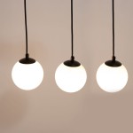 Lampa wisząca Tavira w kolorze czarnym z trzema okrągłymi kloszami ze szkła opalowego, zawieszona na czarnych przewodach. Klosze mają czarne podstawy, a lampa przeznaczona jest do żarówek G9 i GU10.