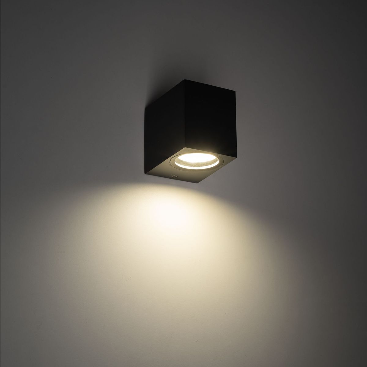 Kinkiet Axis 1xGU10 w kolorze szarym, prostokątny, zamontowany na ścianie. Emituje ciepłe światło w dół, z widoczną oprawą lampy. Prosty design, idealny do nowoczesnych wnętrz. Tło jednolite, co podkreśla produkt.