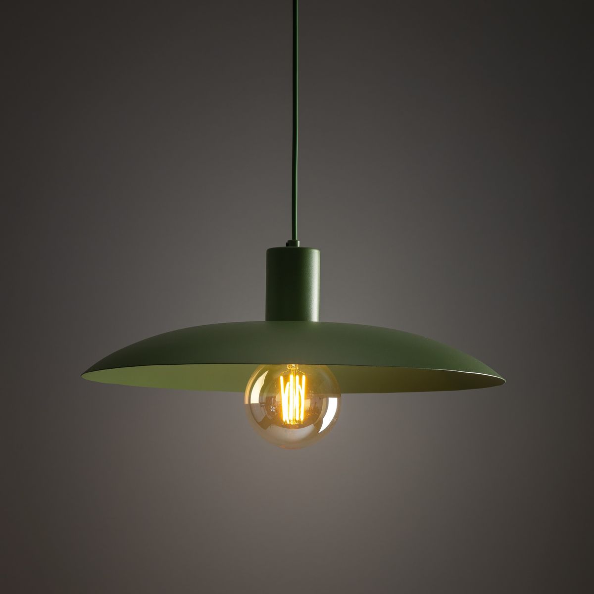 Lampa wisząca Astra 1xE27 w kolorze zielonym, z okrągłym kloszem i transparentną żarówką. Ujęcie z dołu, zawieszona na cienkim przewodzie. Prosty, nowoczesny design, idealna do wnętrz.