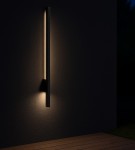 Kinkiet elewacyjny LED 9W w kolorze czarnym, o prostokątnym kształcie, zamontowany na ścianie. Emituje neutralne światło 4000K, z efektem podświetlenia. Tło ciemne, drewniana podłoga w dolnej części zdjęcia. IP44, odpowiedni do użytku na zewnątrz.