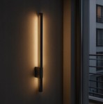 Kinkiet elewacyjny LED 9W w kolorze czarnym, o prostokątnym kształcie, zamontowany na ścianie. Emituje ciepłe, białe światło (4000K) oraz ma stopień ochrony IP44. W tle widoczna szara ściana oraz odcienie cienia.