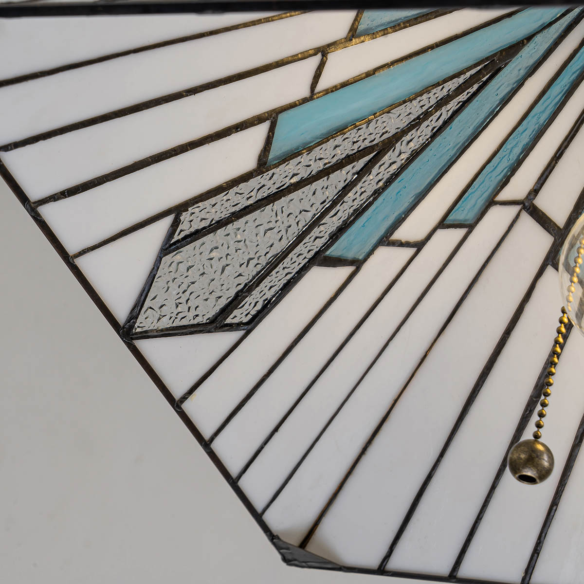 Lampa wisząca Alderley w antycznym brązie z kloszem w formie szklanej mozaiki, w odcieniach białego, szarego i niebieskiego. Widoczne detale w postaci wzorów i struktury szkła, z metalowym łańcuszkiem do włączania.