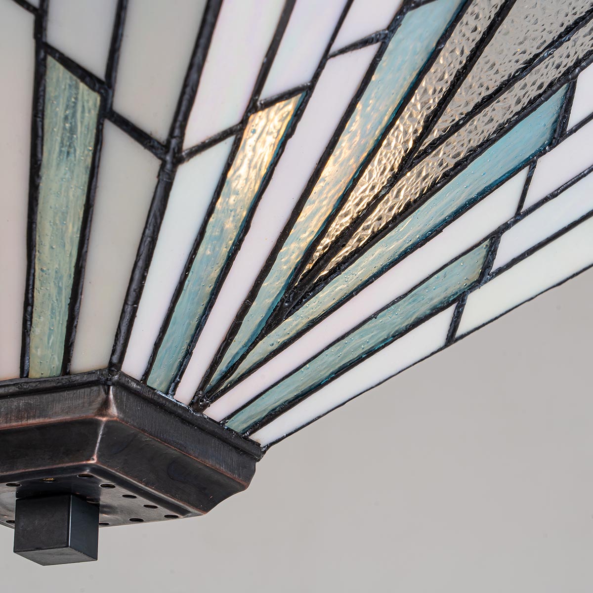 Lampa wisząca Alderley I w antycznym brązie z kloszem z kolorowego szkła w odcieniach bieli i błękitu, o geometrycznym wzorze. Widoczny detal mocowania na suficie, kąt ujęcia zbliżony na górną część klosza.