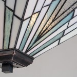 Lampa wisząca Alderley I w antycznym brązie z kloszem z kolorowego szkła w odcieniach bieli i błękitu, o geometrycznym wzorze. Widoczny detal mocowania na suficie, kąt ujęcia zbliżony na górną część klosza.