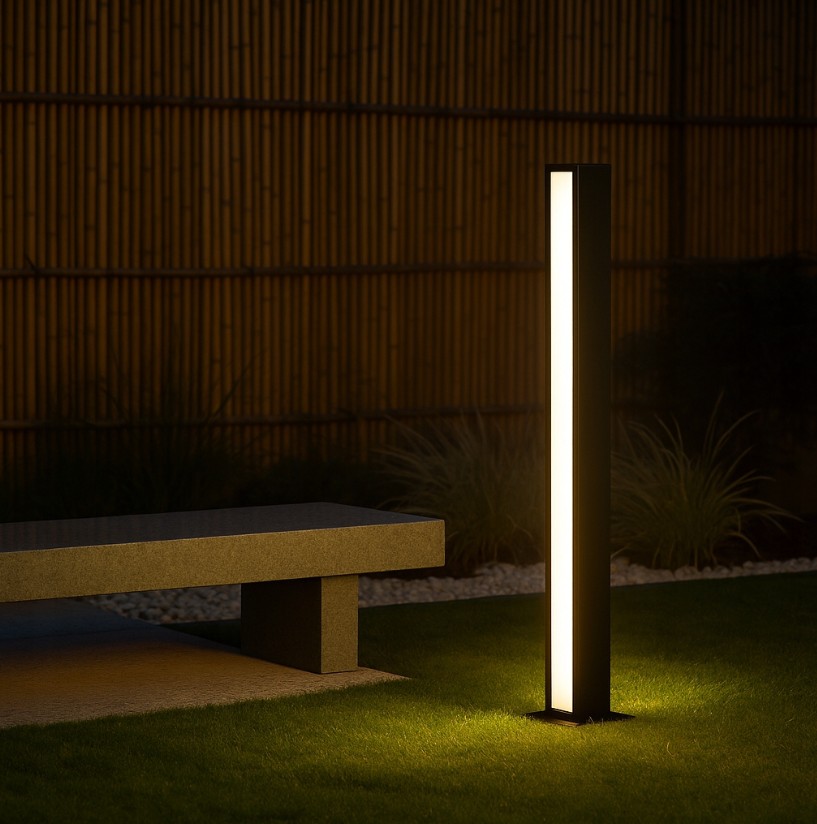 Lampa ogrodowa słupek Roma H60, czarna, o prostokątnym kształcie, z dwoma źródłami LED 24W 4000K. Ustawiona na trawie obok betonowej ławki, emituje ciepłe światło, tworząc przyjemną atmosferę w ogrodzie.