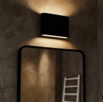 Kinkiet elewacyjny Gantio w kolorze czarnym, z dwoma diodami LED 6W o barwie 4000K, zamontowany na ścianie. Oświetlenie skierowane w górę i w dół, w tle widoczna lustrzana tafla oraz elementy wnętrza.