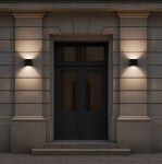 Kinkiet elewacyjny Gantio w kolorze czarnym, z dwoma źródłami LED 6W o temperaturze barwowej 4000K, zamontowany na ścianie obok drzwi. Prosty kwadratowy kształt, iluminacja podkreślająca architekturę budynku. IP44, odporność na warunki atmosferyczne.