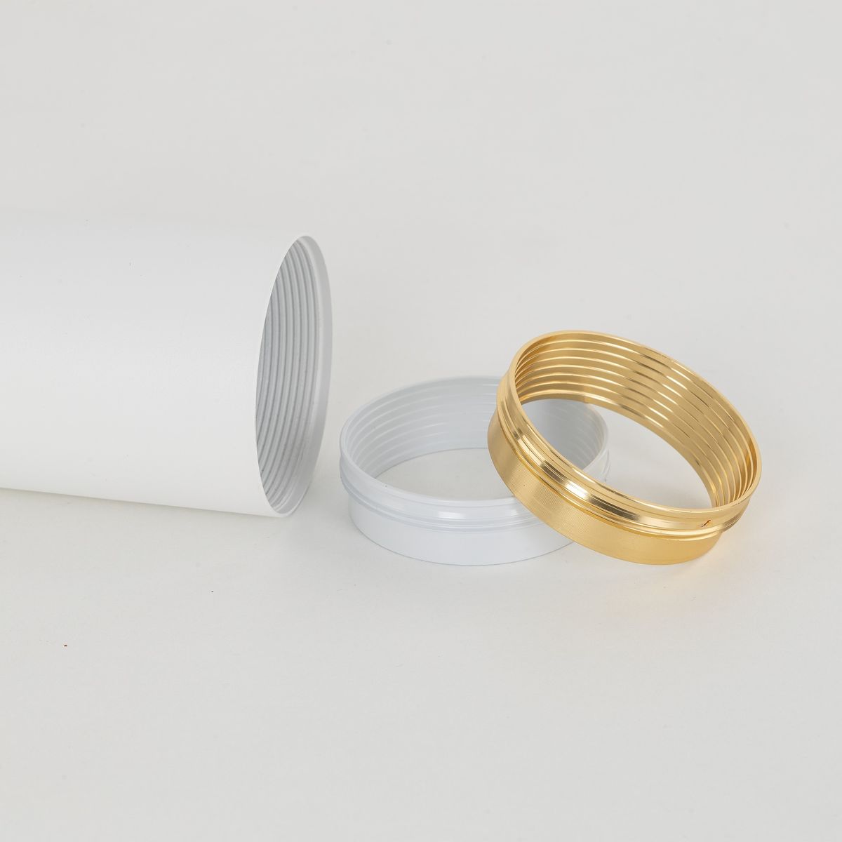 Biała lampa sufitowa Amis z dwoma oprawami GU10. Widoczna biała rurka z gwintem oraz dwa pierścienie: biały i złoty, które mogą służyć do mocowania. Tło jednolite, jasne.