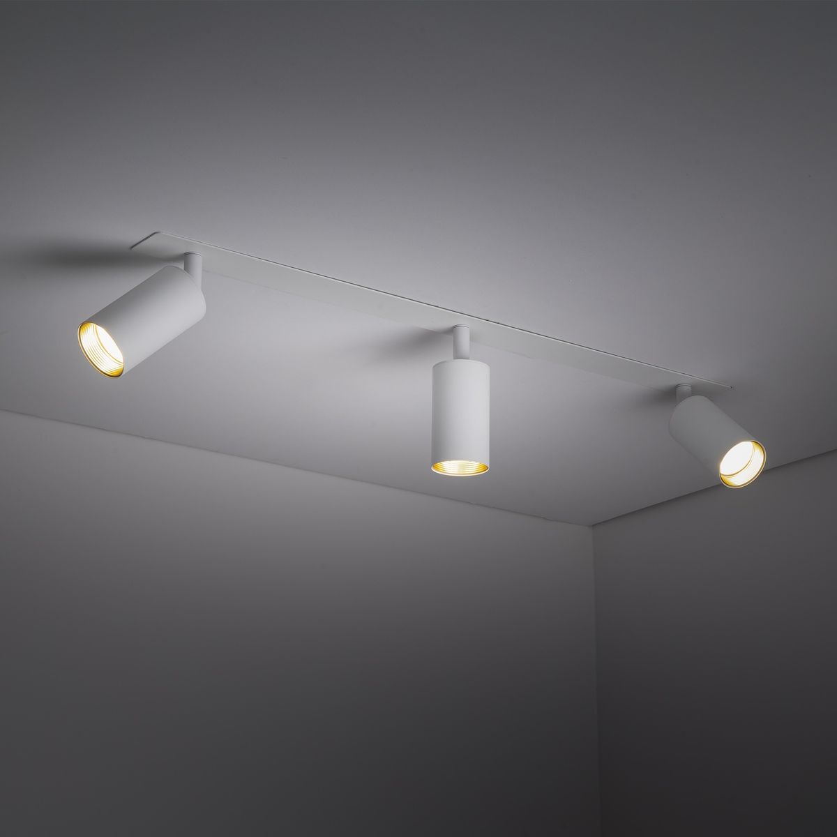 Lampa sufitowa podtynkowa Amis z trzema spotami GU10 w kolorze białym. Montowana w sufit, z cylindrycznymi oprawami skierowanymi w różne strony, podkreślająca nowoczesny styl. Oświetlenie na jednolitym tle.