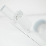 Lampa sufitowa podtynkowa Amis w białym kolorze z trzema oprawami na żarówki GU10. Ujęcie zbliżone na jeden z reflektorów, pokazujące jego cylindryczny kształt i gładką, matową powierzchnię. Na tle jasnej powierzchni, minimalistyczny design.