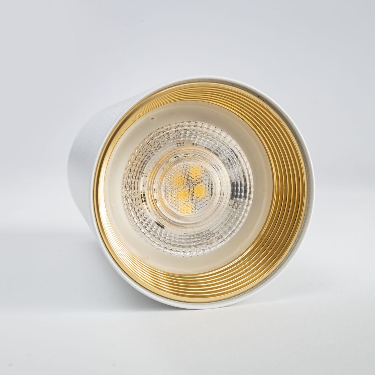 Lampa sufitowa Amis 1xGU10 w kolorze białym z metalicznym wykończeniem w środku. Widok z bliska na źródło światła, z przezroczystą osłoną i wypukłym wzorem, z widocznymi żarówkami LED. Kształt cylindryczny, montaż sufitowy.