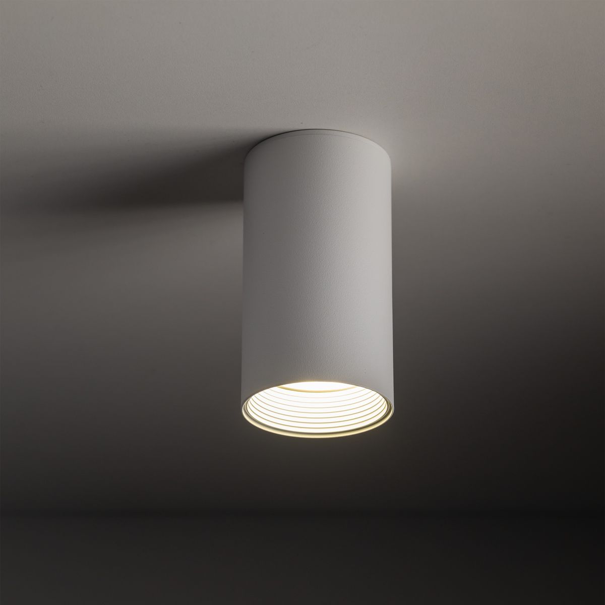 Lampa sufitowa Amis 1xGU10 w kolorze białym, cylindryczna, z widocznym kloszem z żłobieniami u góry. Zawieszona w pozycji pionowej, na jednolitym tle, emitująca ciepłe światło. Idealna do nowoczesnych wnętrz.