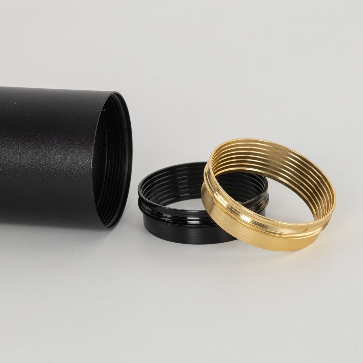 Czarna lampa sufitowa Amis z oprawą na żarówkę GU10, widok z boku. Obok znajdują się dwie pierścienie: czarny i złoty, z widocznymi gwintami. Tło jasnoszare, minimalistyczne.