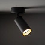 Lampa sufitowa Amis w kolorze czarnym z jednym gniazdem GU10. Ujęcie z boku, pokazujące cylindryczny klosz z odsłoniętym żarnikiem. Elementy metalowe, matowe wykończenie, montowana do sufitu.