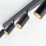 Lampa sufitowa Amis w kolorze czarnym z czterema reflektorami GU10. Reflektory mają cylindryczny kształt, z widocznymi złotymi wnętrzami. Ujęcie z boku, ukazujące część konstrukcji przymocowanej do sufitu. Tło białe.